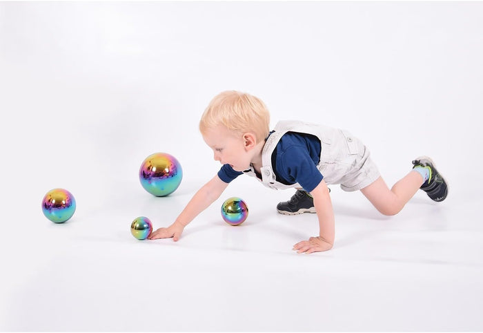 Child reaching for four shiny, iridescent spheres of varying sizes with a rainbow-colored reflective finish.