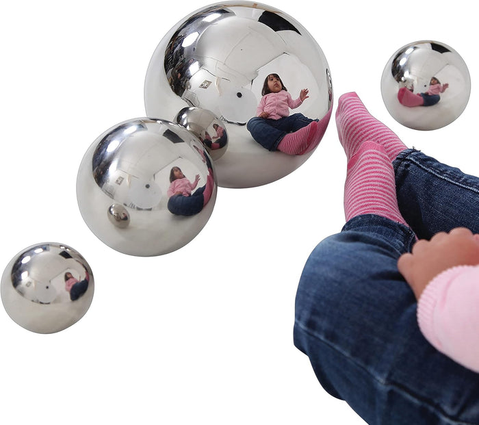 Reflective silver spheres in various sizes showing a child's reflection against a plain white background.
