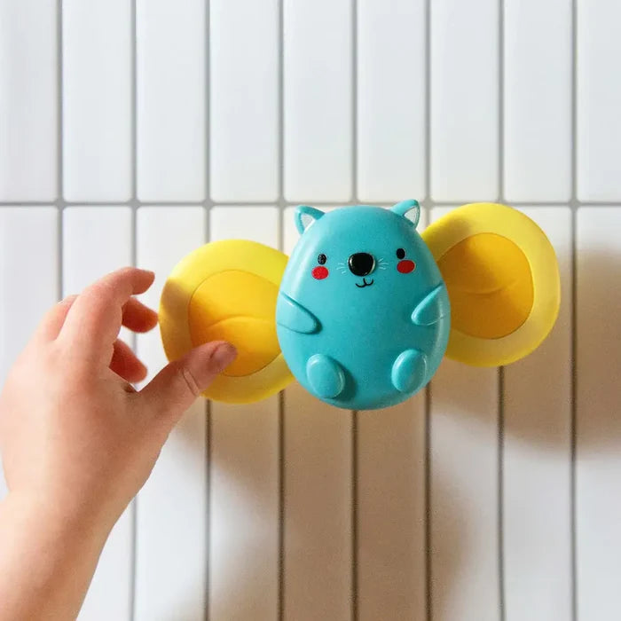 Blue koala sensory spinner with yellow rotating wings on a tiled wall, being touched by a hand.