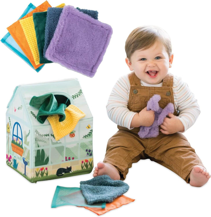 Smiling baby playing with colorful textured fabric squares from a soft, garden-themed house-shaped toy box.