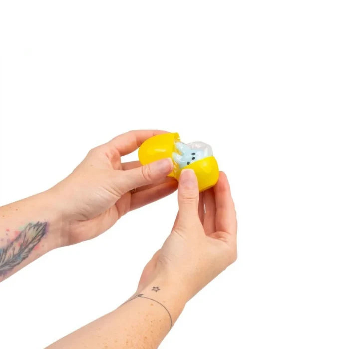 Hands opening a small yellow plastic capsule to reveal a blue squishy sensory toy inside.