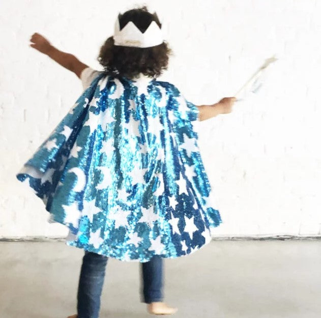 Child from behind wearing a blue sequin cape with white star and moon patterns, a white crown, and holding a wand.