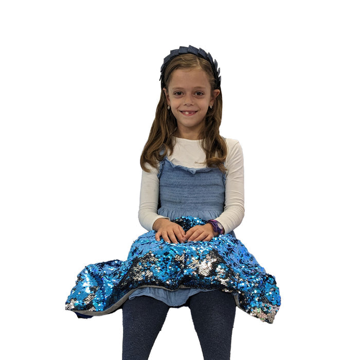 A child sitting with a shimmering blue and silver reversible sequined pad resting on their lap.