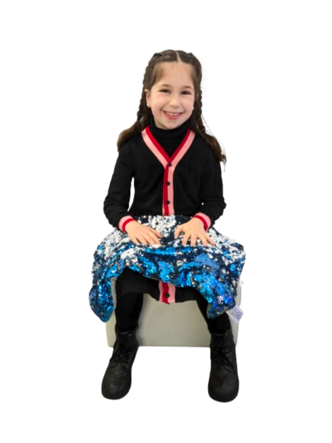 A young girl sitting with a shimmering blue and silver sequined weighted lap pad draped across her legs.
