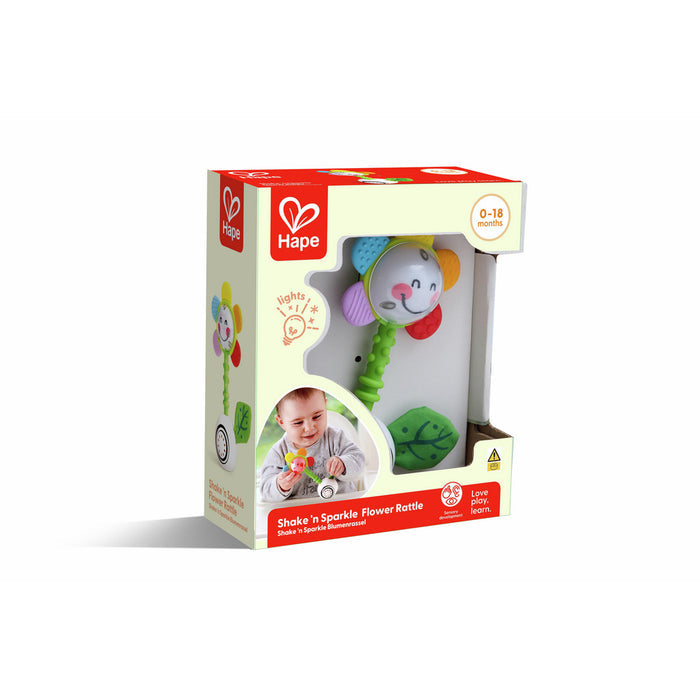Hape flower rattle in box. Features colorful petals, smiley face, green textured handle, and green fabric leaf.