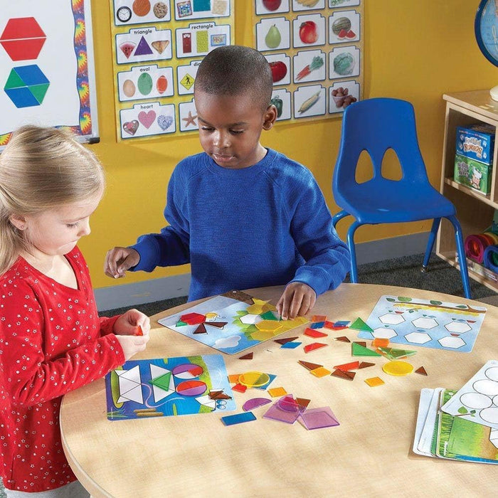 Two children at a table using translucent geometric shapes to complete patterns on bug-themed activity cards.