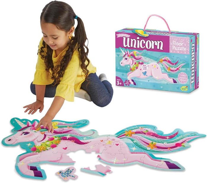 Child assembling a large pink shimmery unicorn floor puzzle with floral details next to its colorful storage box.