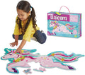 Child assembling a large pink shimmery unicorn floor puzzle with floral details next to its colorful storage box.