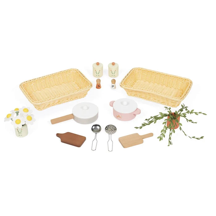 Pastel toy kitchen set with yellow woven baskets, pink pot, white pan, wooden utensils, salt and pepper shakers, and plants.