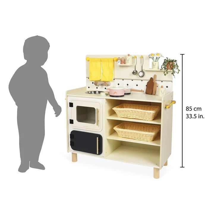 Wooden play kitchen with a white oven, woven baskets, yellow curtains, and accessories. Height is 85cm.