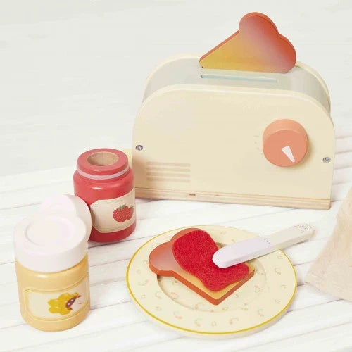 Cream wooden toy toaster with heart toast, red jam and yellow honey jars, plus toast on a plate with a spreader.