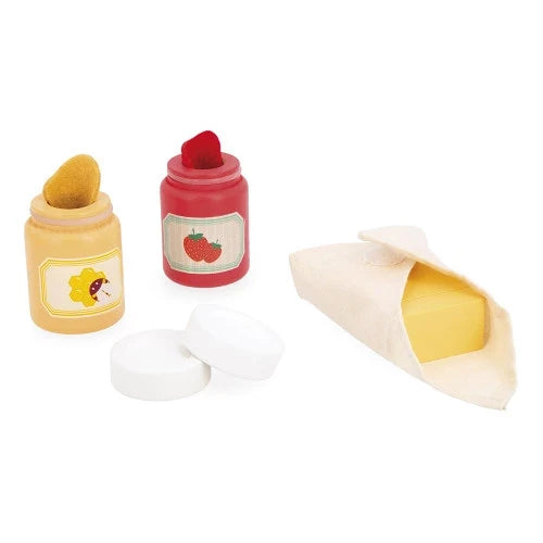 Toy red strawberry jam and yellow honey jars with lids beside a wooden butter block in a cream fabric wrap.