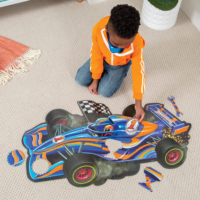 A child assembles a glossy blue and orange racecar floor puzzle with uniquely shaped pieces on a beige carpet.