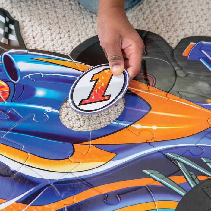 Hand placing a shiny circular number 1 piece into a large blue and orange racecar floor puzzle.