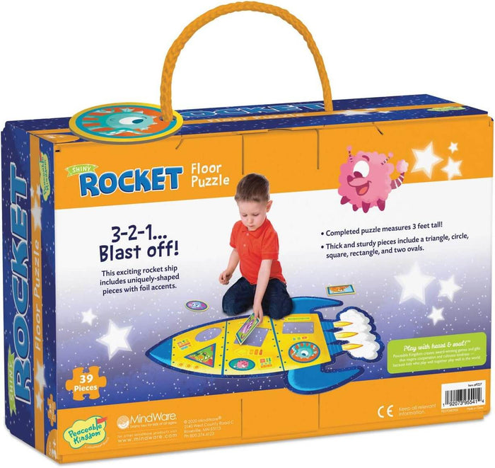 Orange box with rope handle showing a boy building a large blue rocket floor puzzle with 39 shiny, shaped pieces.