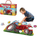 A boy assembles a large red tractor-shaped floor puzzle with farm animals next to its colorful storage box.