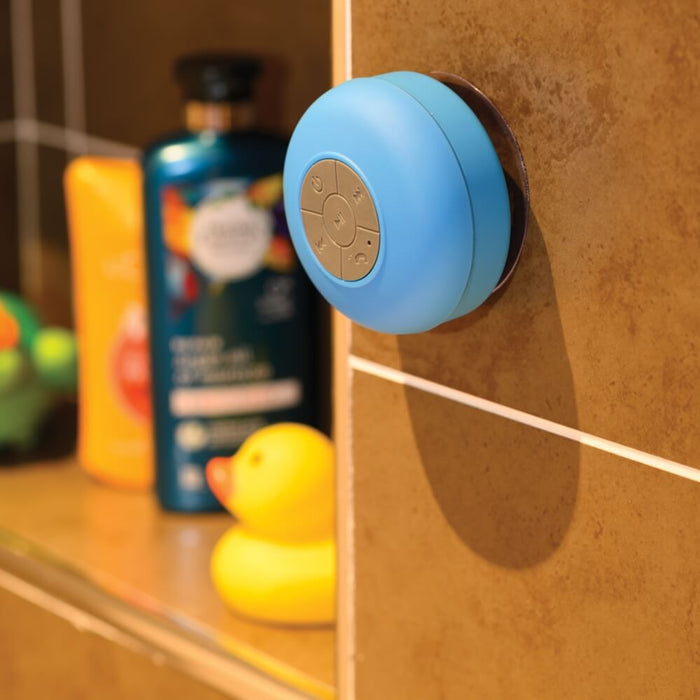 Blue round speaker with grey buttons suctioned to a brown tile wall, with a yellow rubber duck in the background.