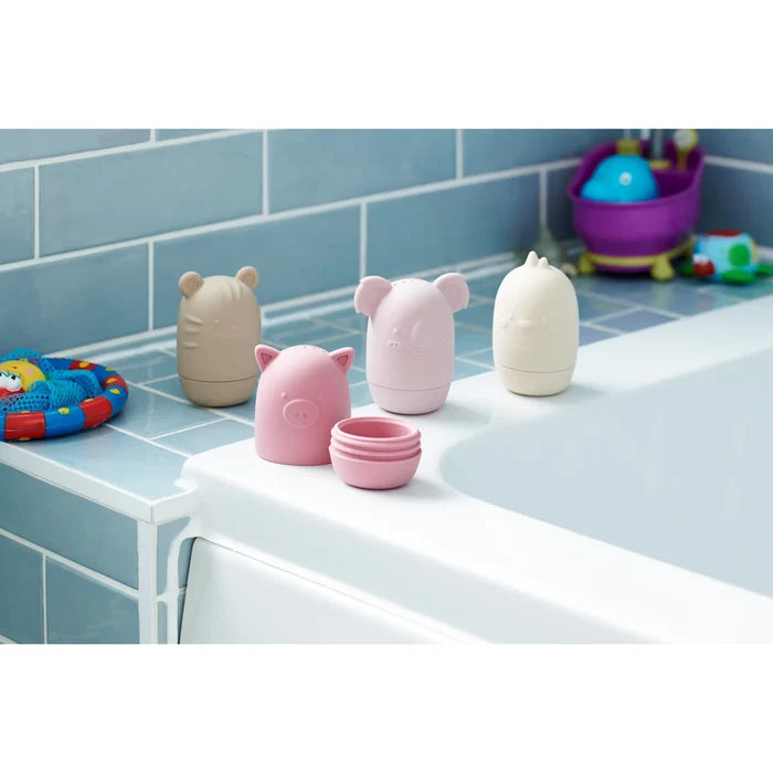 Four pastel silicone animal bath toys on a tub edge; the pink pig toy is unscrewed to show its two-piece design.