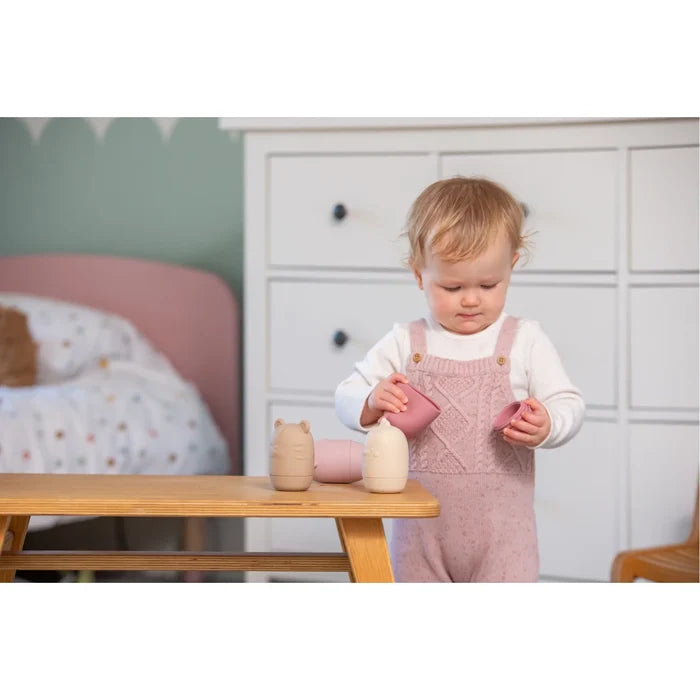 Toddler playing with soft pink and beige silicone animal-shaped toys on a small wooden table in a nursery.