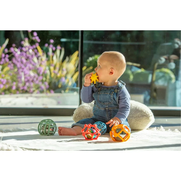 Baby plays on a rug with five colorful, open-framed silicone balls in green, red, blue, yellow, and orange.