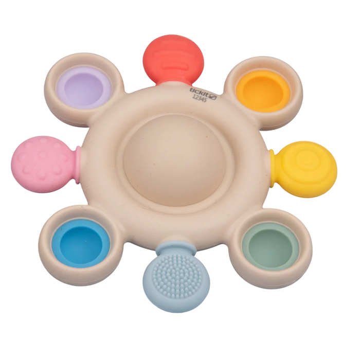 Beige circular silicone teether with colorful pop bubbles and textured sensory tabs around the perimeter.