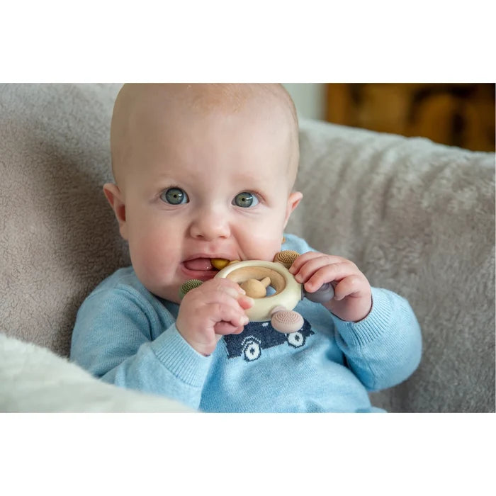 Baby chewing on a round teether with a wooden ring and earth-toned textured silicone knobs.