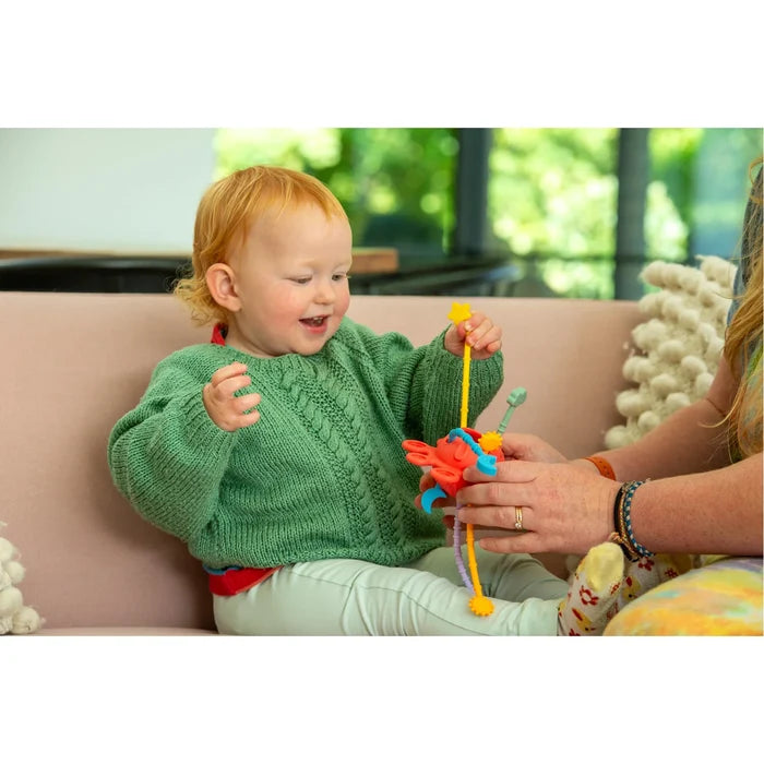 Red-haired toddler pulls on a colorful octopus-shaped silicone activity toy with flexible, textured cords.