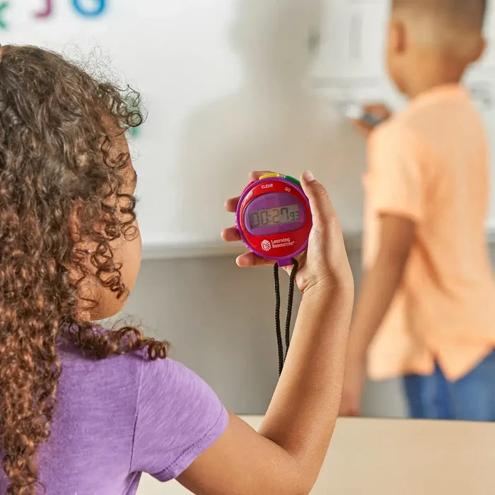 Purple and red digital stopwatch with colorful buttons and a black lanyard held by a student in a classroom.