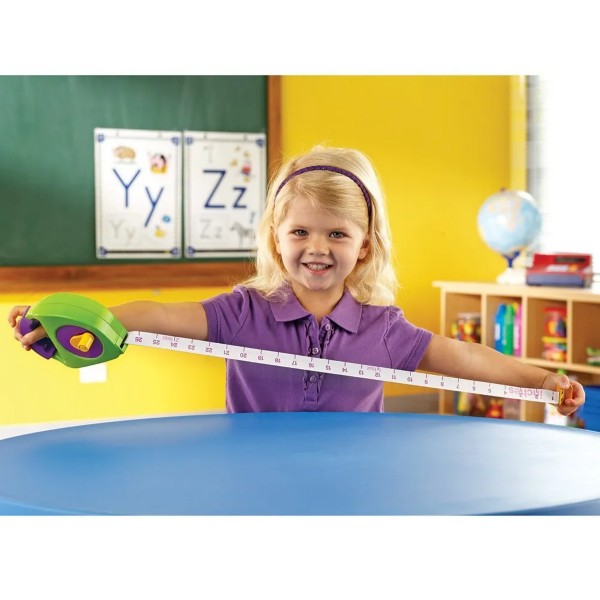 Child holds a chunky green and purple plastic tape measure with large numbers on a long white measuring tape.