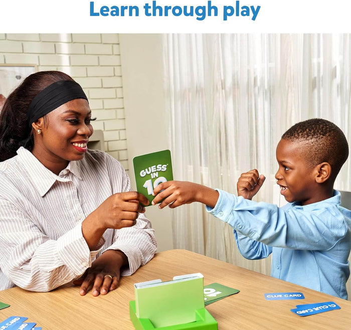 A woman and young boy smile and play a Skillmatics Guess in 10 green card game at a table.