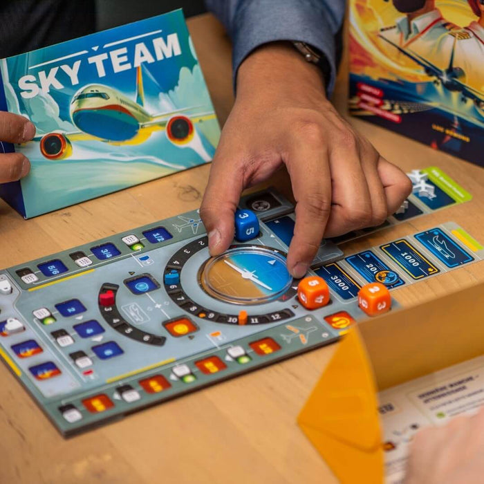 Hands placing dice on a cockpit-themed game board next to the Sky Team box with an airplane illustration.