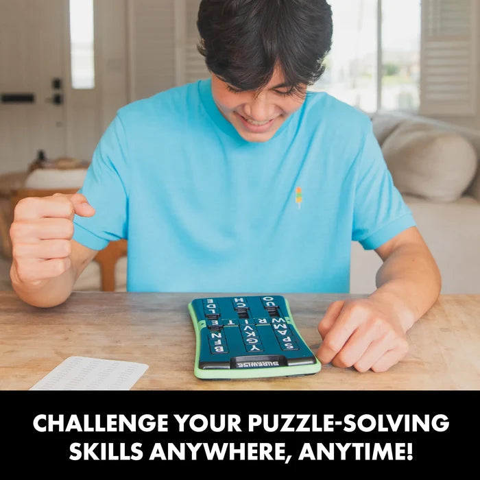 Smiling man playing a green and black handheld puzzle game with sliding letter tiles on a wooden table.