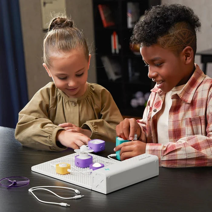 Two children building a circuit using colorful modular blocks, white cables, and a pegboard base.