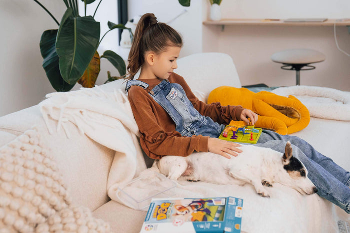 Girl playing Smart Dog game with colorful obstacles on a yellow board, sitting on a sofa with her pet dog.