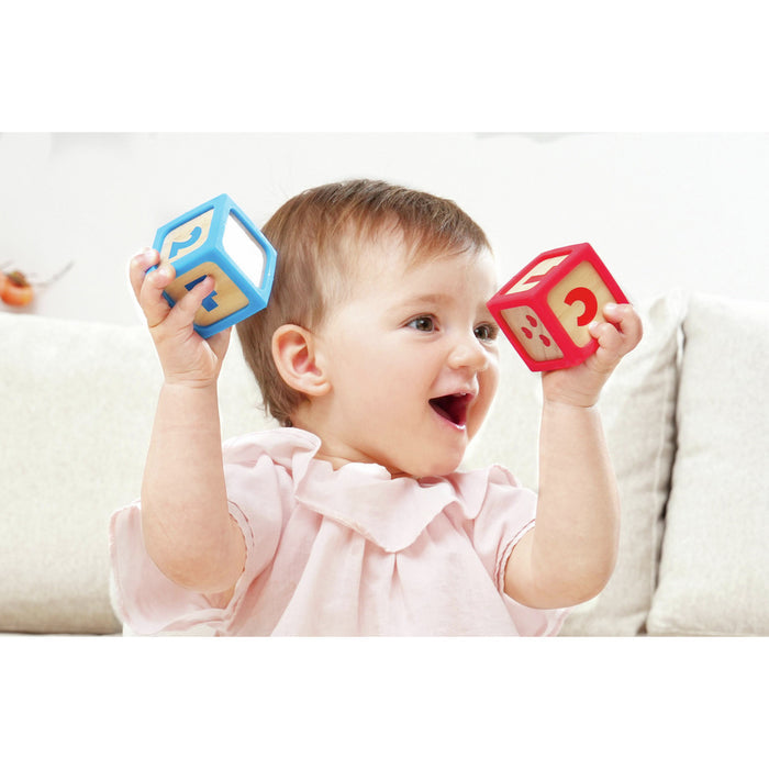 Smiling baby holds two wooden square blocks with colorful soft frames featuring numbers and symbols.