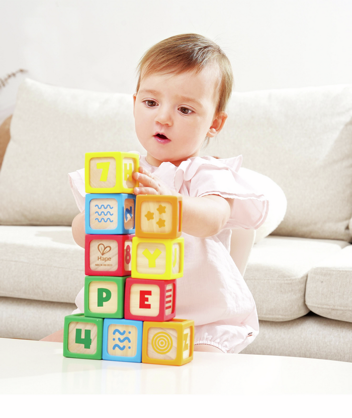 Baby stacking colorful wooden blocks featuring letters, numbers, and symbols in bright red, blue, yellow, and green.