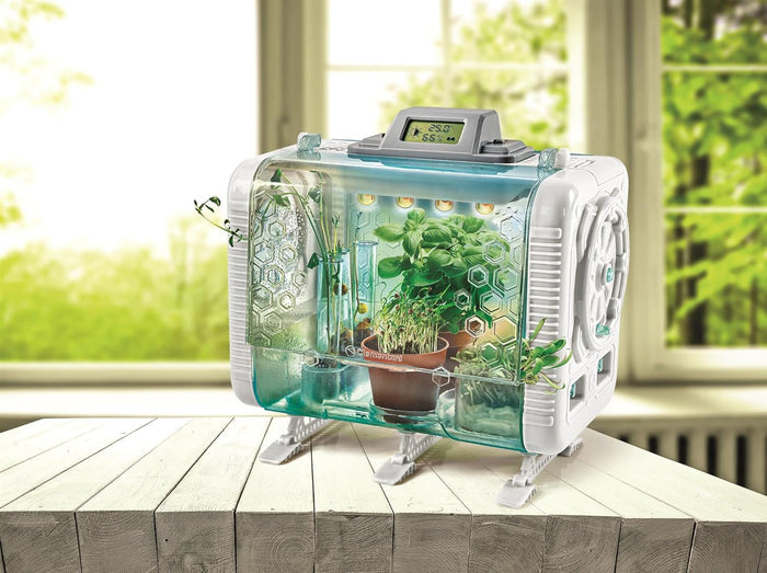 Futuristic white toy greenhouse with digital display, LED lights, and small plants visible inside clear blue walls.