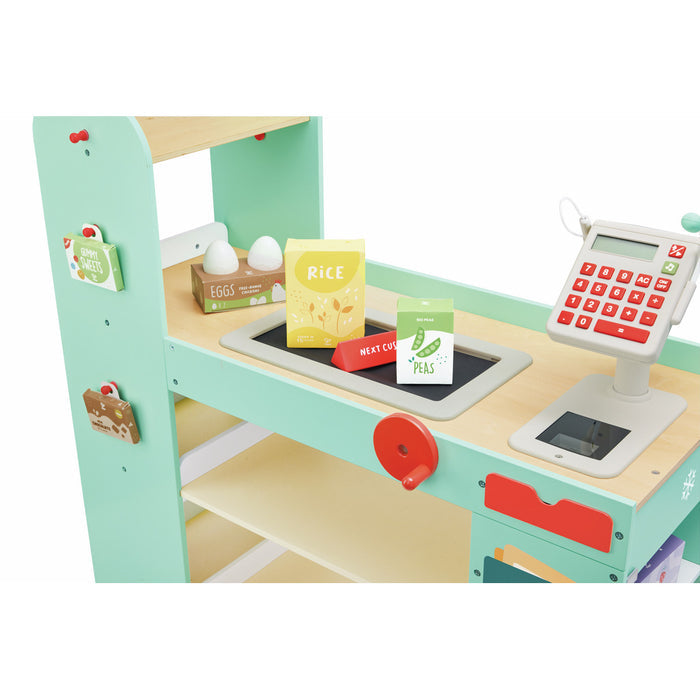 Mint green wooden play shop featuring a cash register, conveyor belt, and toy groceries like eggs, rice, and peas.