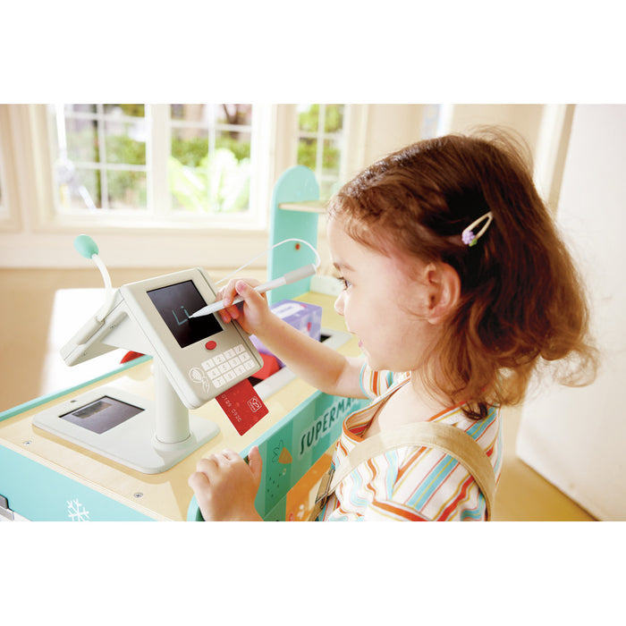 Young girl using a stylus on a white and teal wooden toy cash register with a red play credit card.