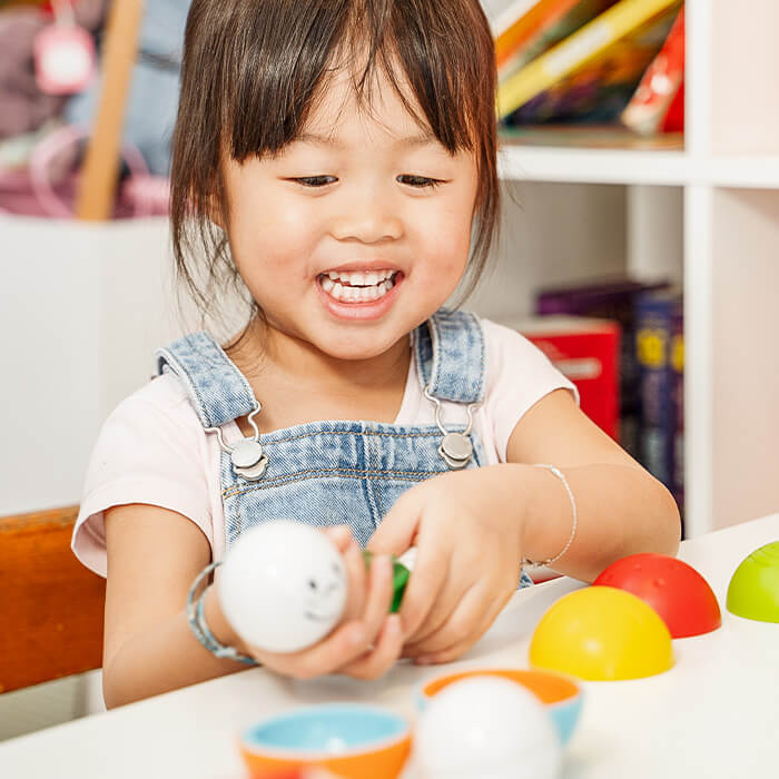 Smiling child playing with colorful magnetic hemisphere caps and a white sphere with a face.