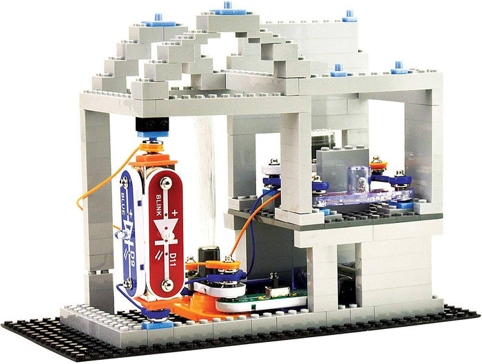 Grey toy building made of bricks with integrated red and blue electronic circuits and orange wires on a black baseplate.