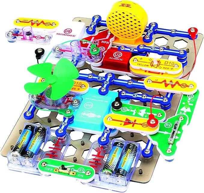 Colorful electronics kit on a grey grid featuring a green fan, yellow speaker, and blue snap connectors.