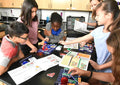 Diverse students building electronic circuits using colorful snap-together parts, blue grids, and open manuals.