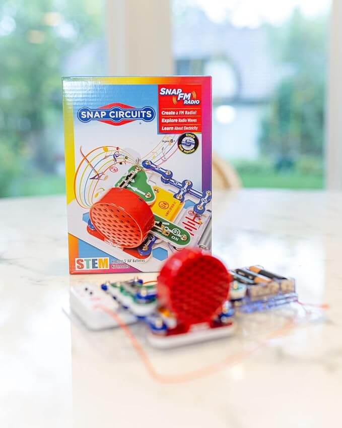 Colorful Snap Circuits FM Radio box next to an assembled model with a red speaker and blue snap-together pieces.