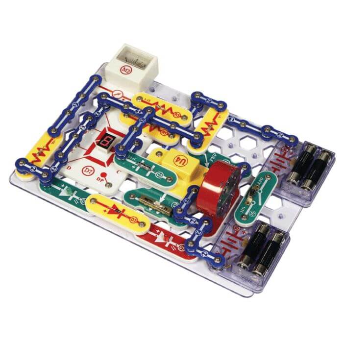 Electronic circuit kit with colorful snap-on components, a meter, and battery packs on a clear plastic grid base.