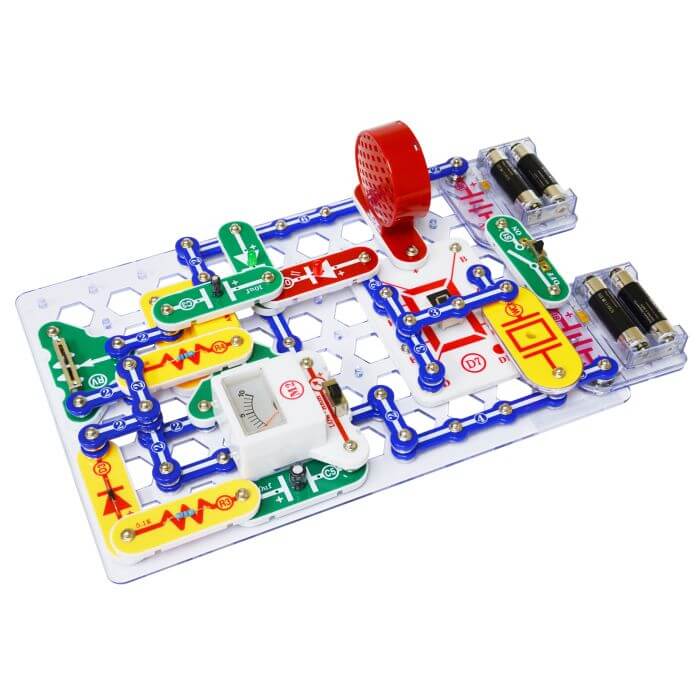 Colorful electronic circuit with a red speaker, batteries, and a meter assembled on a white plastic grid base.