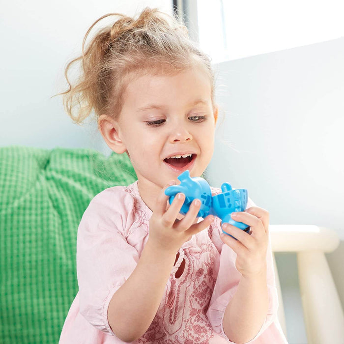 A young girl smiles while snapping together two pieces of a bright blue plastic dinosaur toy.