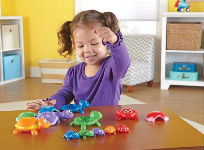 Child playing with colorful, snap-together plastic turtle toys in blue, green, orange, and purple on a wooden table.