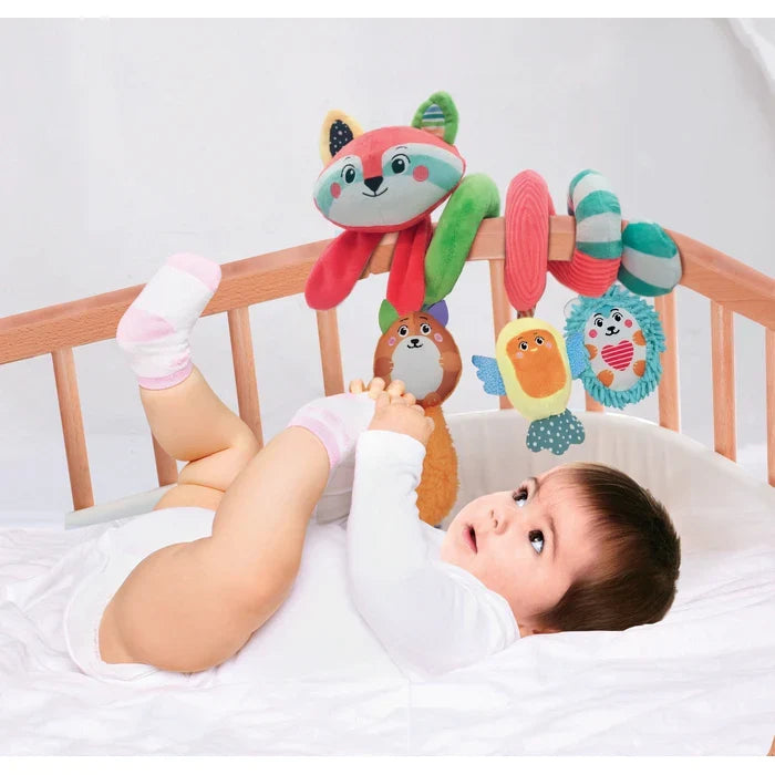 Baby in a wooden crib looking at a colorful plush spiral toy with a red fox head and hanging animal characters.
