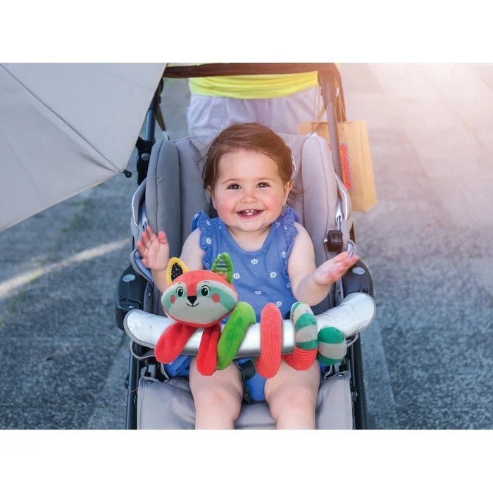 Red and green plush fox spiral toy wrapped around a stroller's bumper bar with a smiling baby sitting inside.